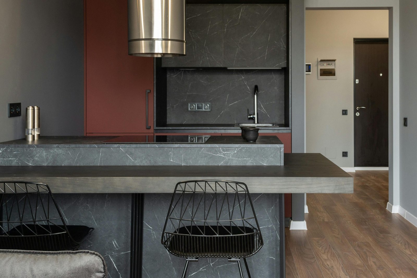 Dining zone furnished with counter and chairs in modern apartment with island style kitchen equipped with range hood and illuminated by hanging lamps