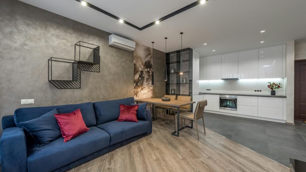 Comfortable blue sofa with soft pillows placed near dining table in cozy spacious apartment with kitchen area